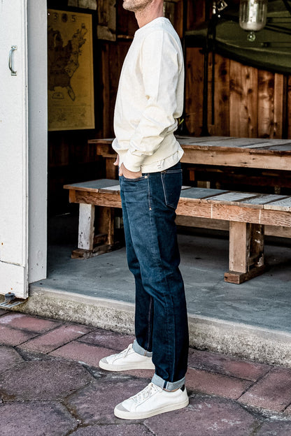 Side view of dark ocean wash American made denim jeans with cuffed hem, paired with cream sweatshirt and white sneakers.