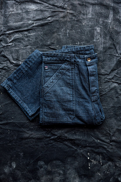 Women’s premium denim jeans folded neatly on a dark textured surface, showcasing rich blue fabric, structured seams, and front utility pocket detailing
