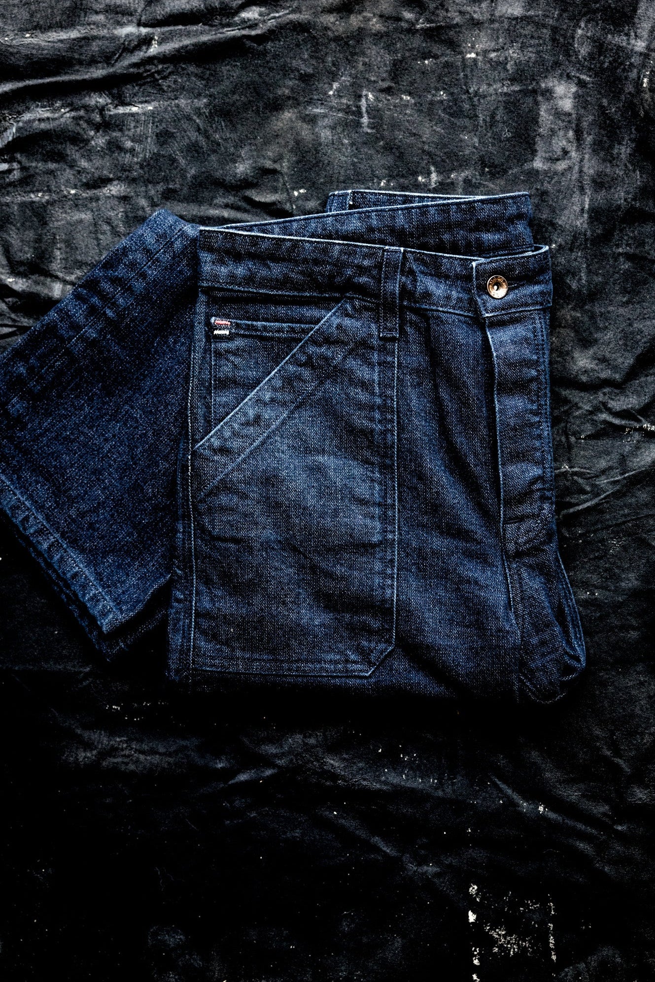 WiesMade Scout jeans in ocean indigo folded on a dark textured surface, showing back pocket and yoke.
