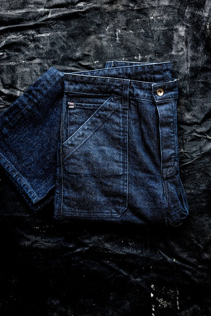 WiesMade Scout jeans in ocean indigo folded on a dark textured surface, showing back pocket and yoke.