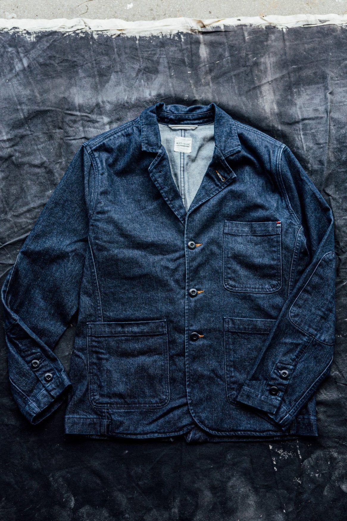 Ocean blue denim chore blazer laid flat, showing notched lapels, patch pockets, and buttoned cuffs.