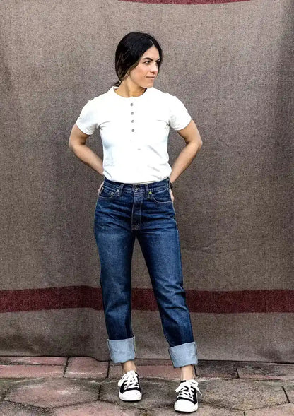 Woman in high-rise straight-leg selvedge denim jeans with cuffed hems, paired with a white henley and sneakers.