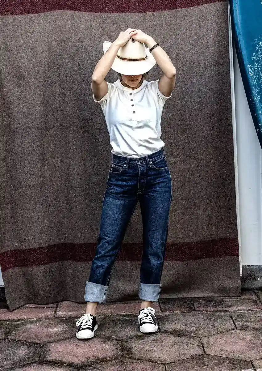 High rise straight leg selvedge denim jeans with cuffed hems, styled with a white henley and straw hat.