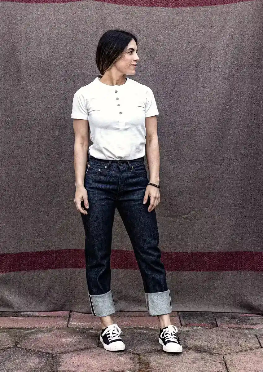Model wearing high-rise raw selvedge denim jeans with cuffed hems, paired with a white henley tee and sneakers.