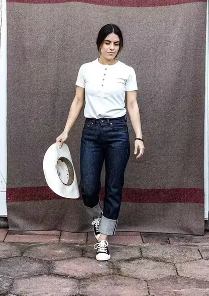 High-rise raw selvedge denim jeans with cuffed hem, paired with a white tee and sneakers.