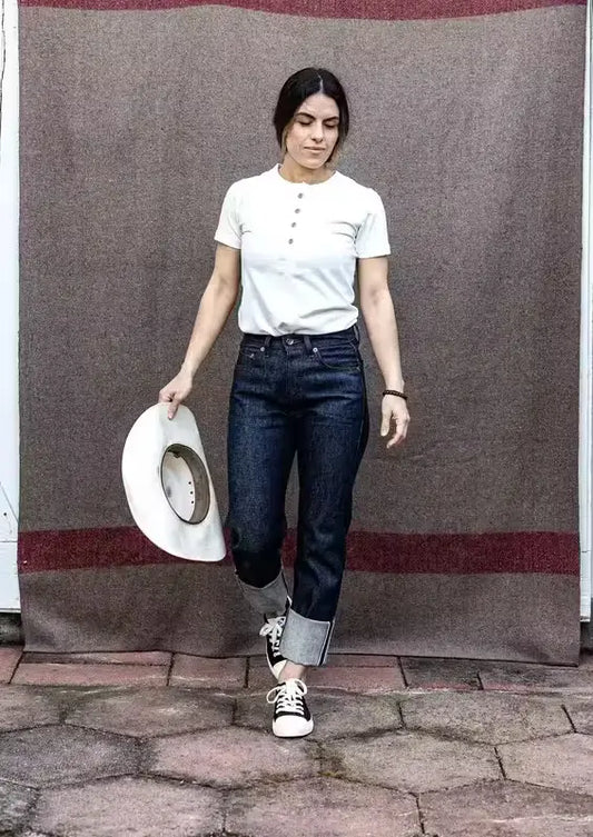 High-rise raw selvedge denim jeans with cuffed hem, paired with a white tee and sneakers.