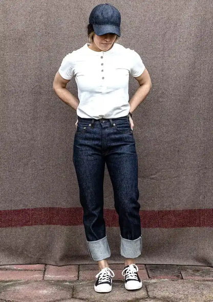 Sidney high-rise raw selvedge denim jeans with cuffed hems, styled with a white henley tee and denim cap.