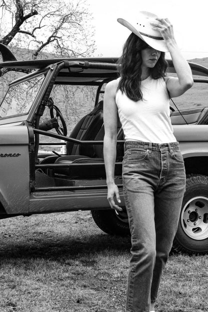 Model in salt wash high-rise straight leg jeans and white tank, wearing a cowboy hat beside a vintage Bronco.
