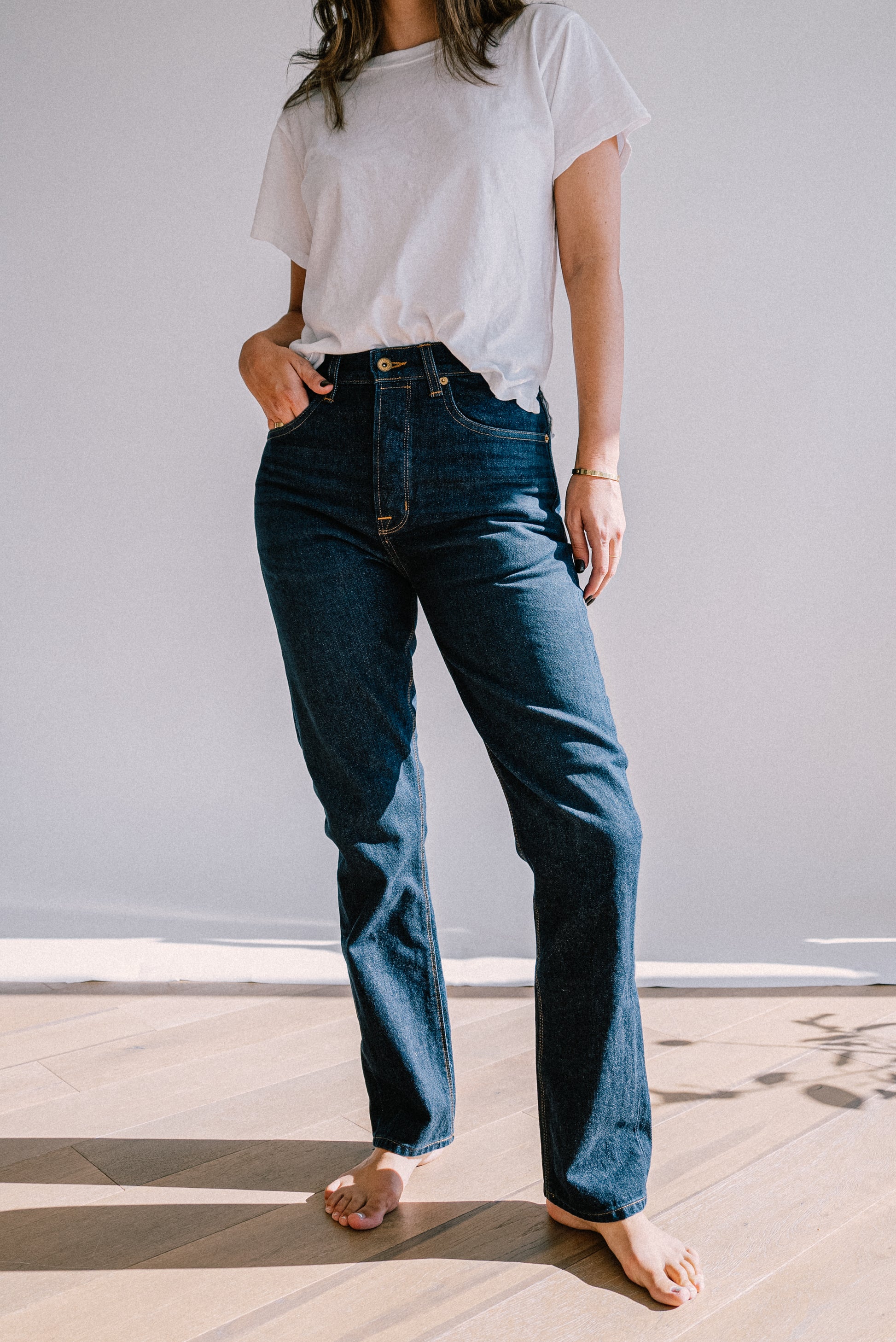 Model wearing high-rise straight-leg American made jeans in dark ocean wash denim with a white tee.