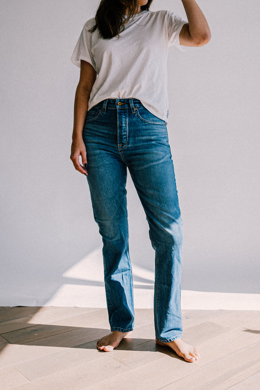 Model in salt wash high-rise straight-leg American made jeans and a white tee, barefoot in sunlight.