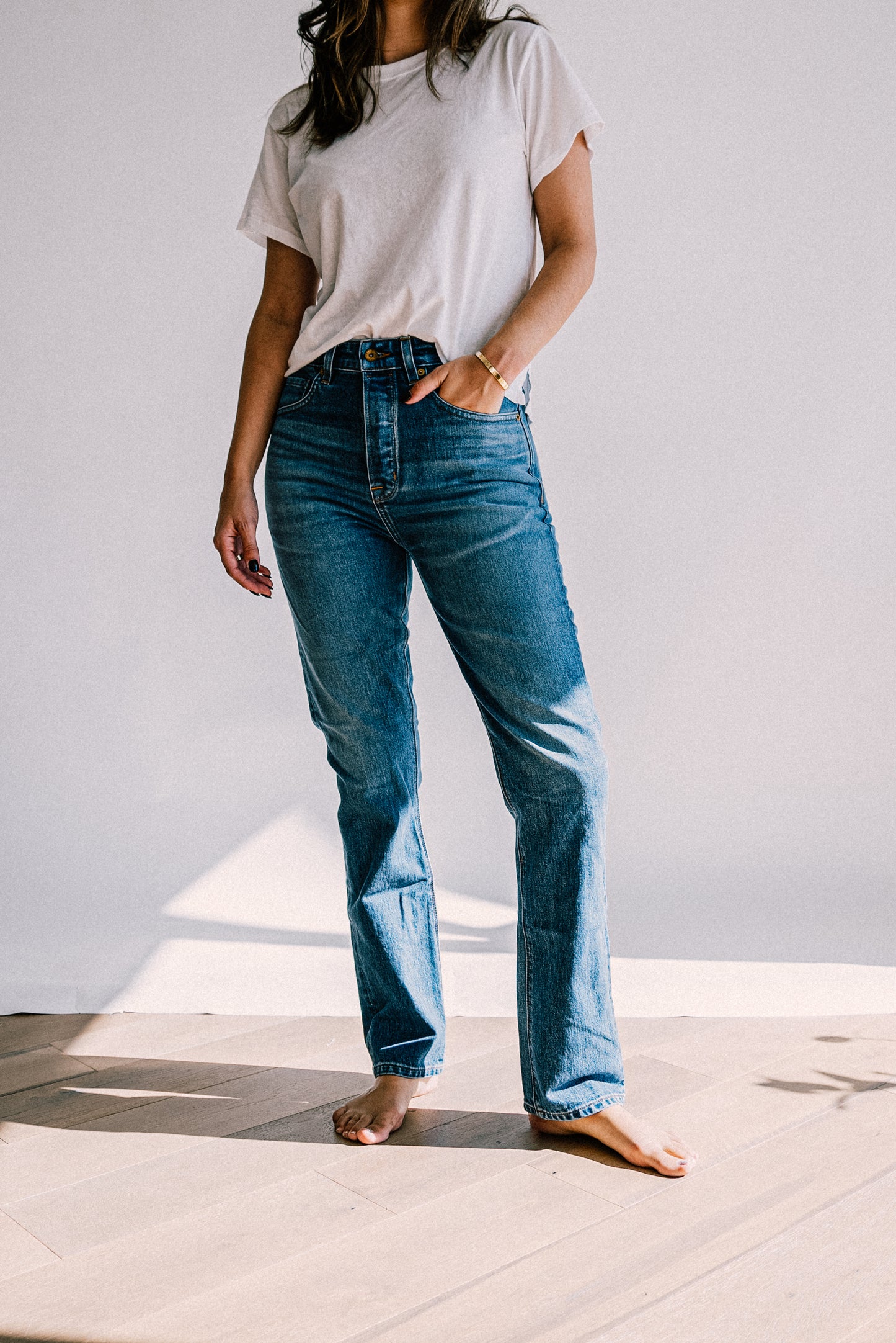 High-rise straight-leg salt wash American made jeans styled with a white tee, shown barefoot in sunlight.