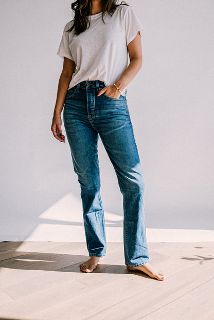 High-rise straight-leg salt wash American made jeans styled with a white tee, shown barefoot in sunlight.