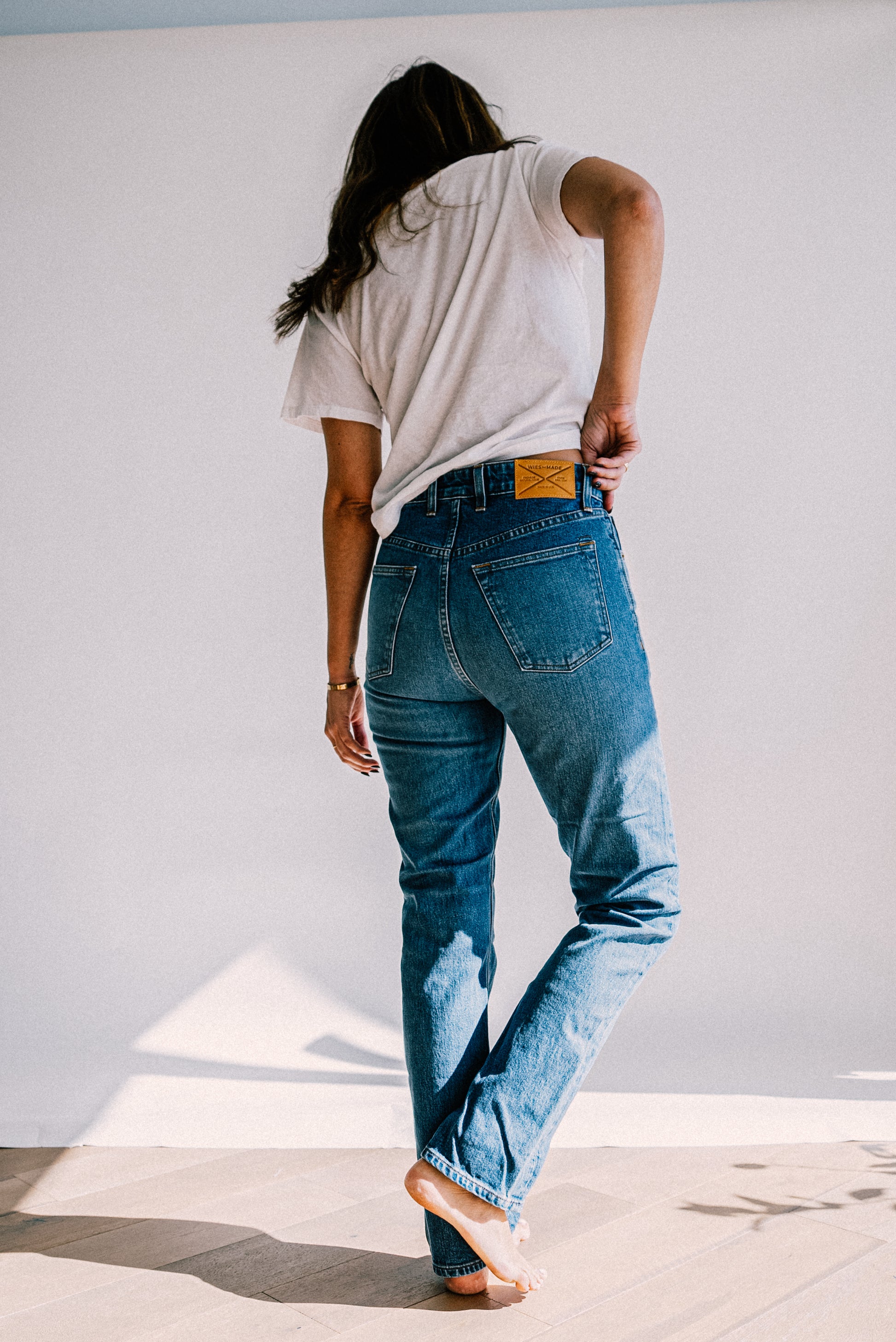 Back view of salt wash high-rise straight leg jeans with leather WiesMade patch, worn with a white tee.