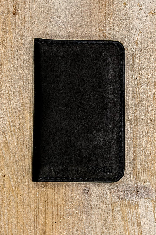 Black Horween leather bifold wallet with embossed WM logo on weathered wood.