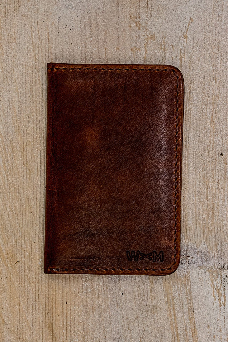 Tan Horween leather small wallet, hand-stitched, stamped with WM logo on weathered wood.