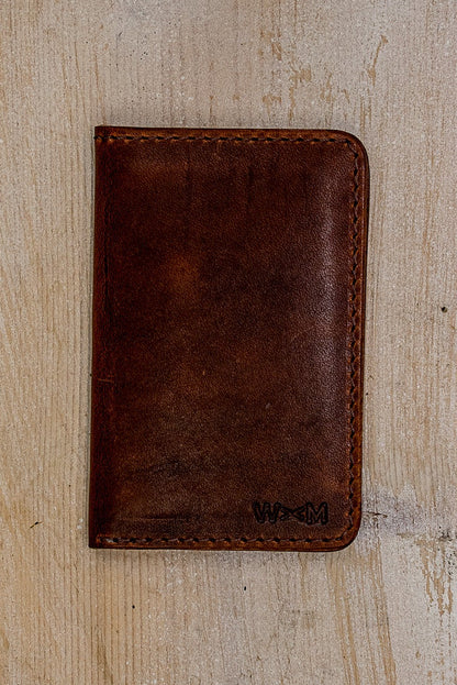 Tan Horween leather small wallet, hand-stitched, stamped with WM logo on weathered wood.