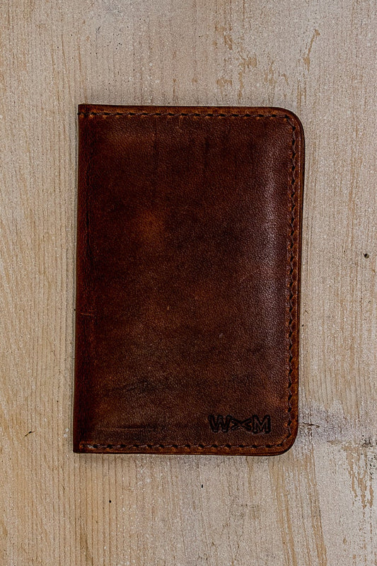 Tan Horween leather small wallet, hand-stitched, stamped with WM logo on weathered wood.