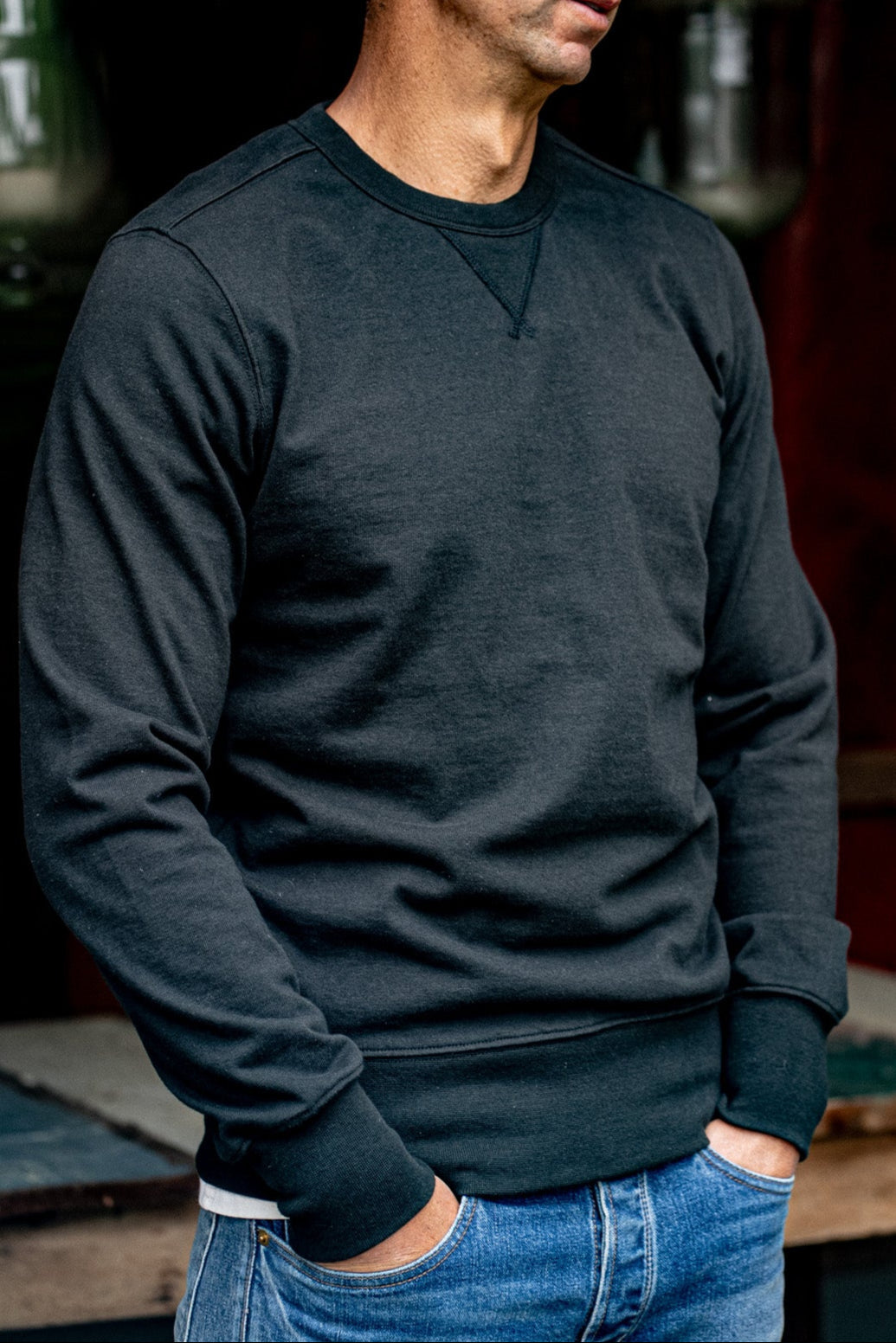 Man wearing a basalt black Stinson rugby jersey pullover with V-stitch detail, paired with blue denim jeans.