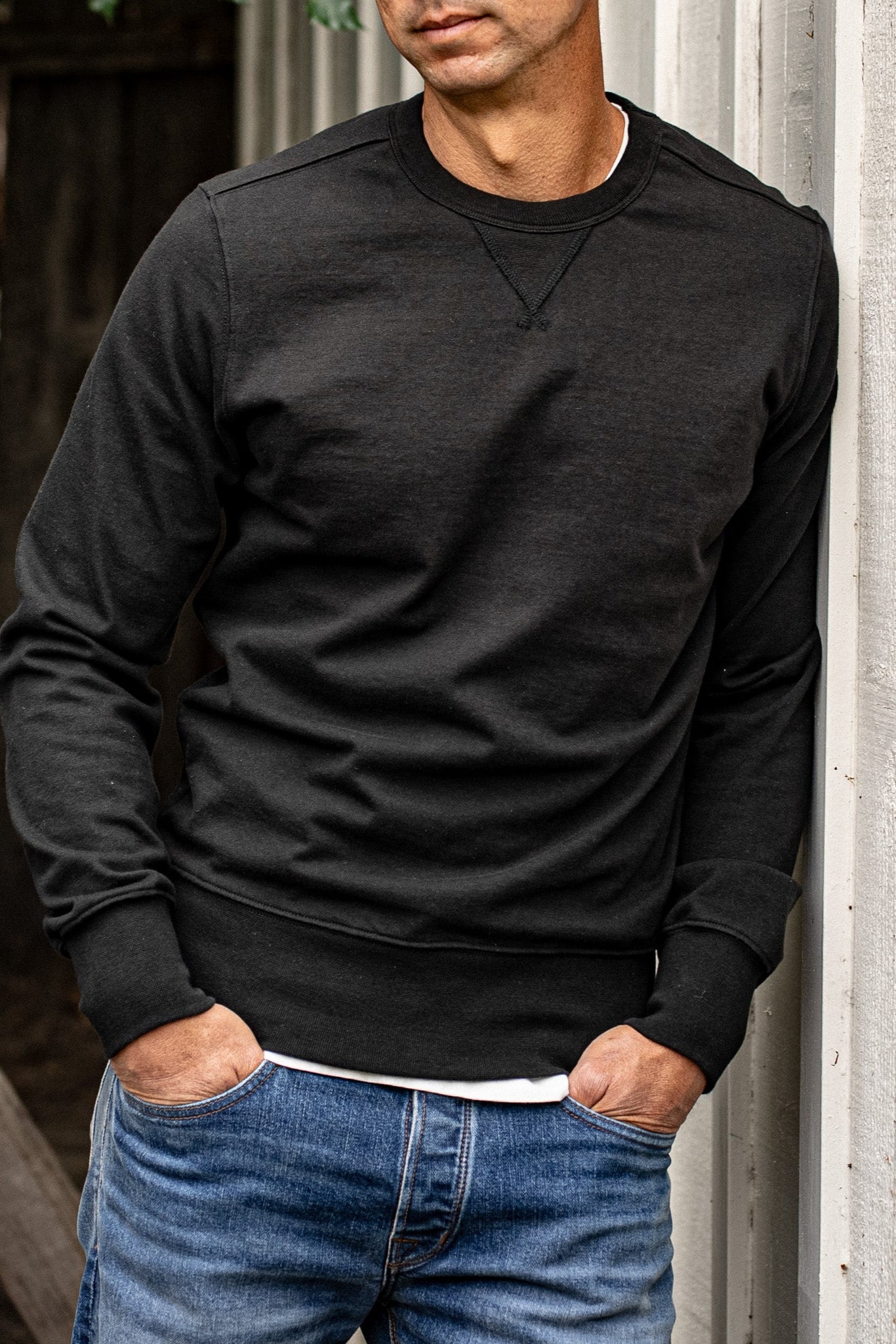 Men's Stinson rugby jersey pullover in basalt black, worn with blue denim jeans against a weathered wood wall.
