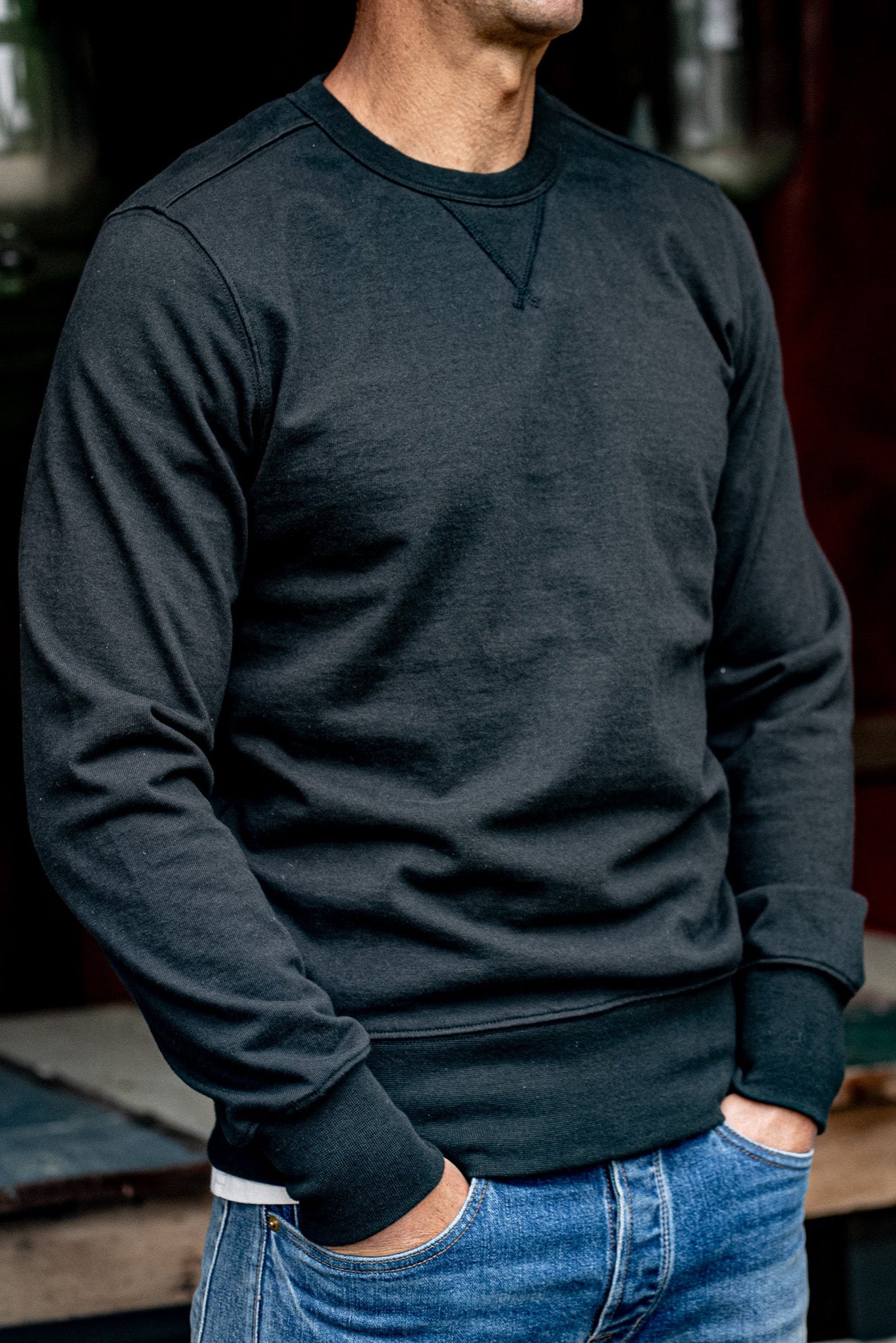 Man wearing the basalt Stinson crewneck pullover with blue jeans, showing the V-stitch detail at the neckline.