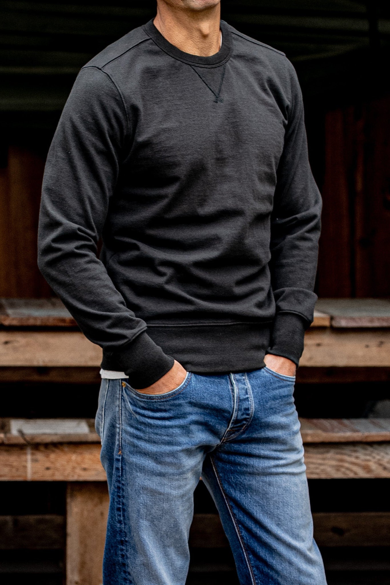 Man wearing basalt Stinson rugby jersey pullover with blue jeans by a wooden barn.