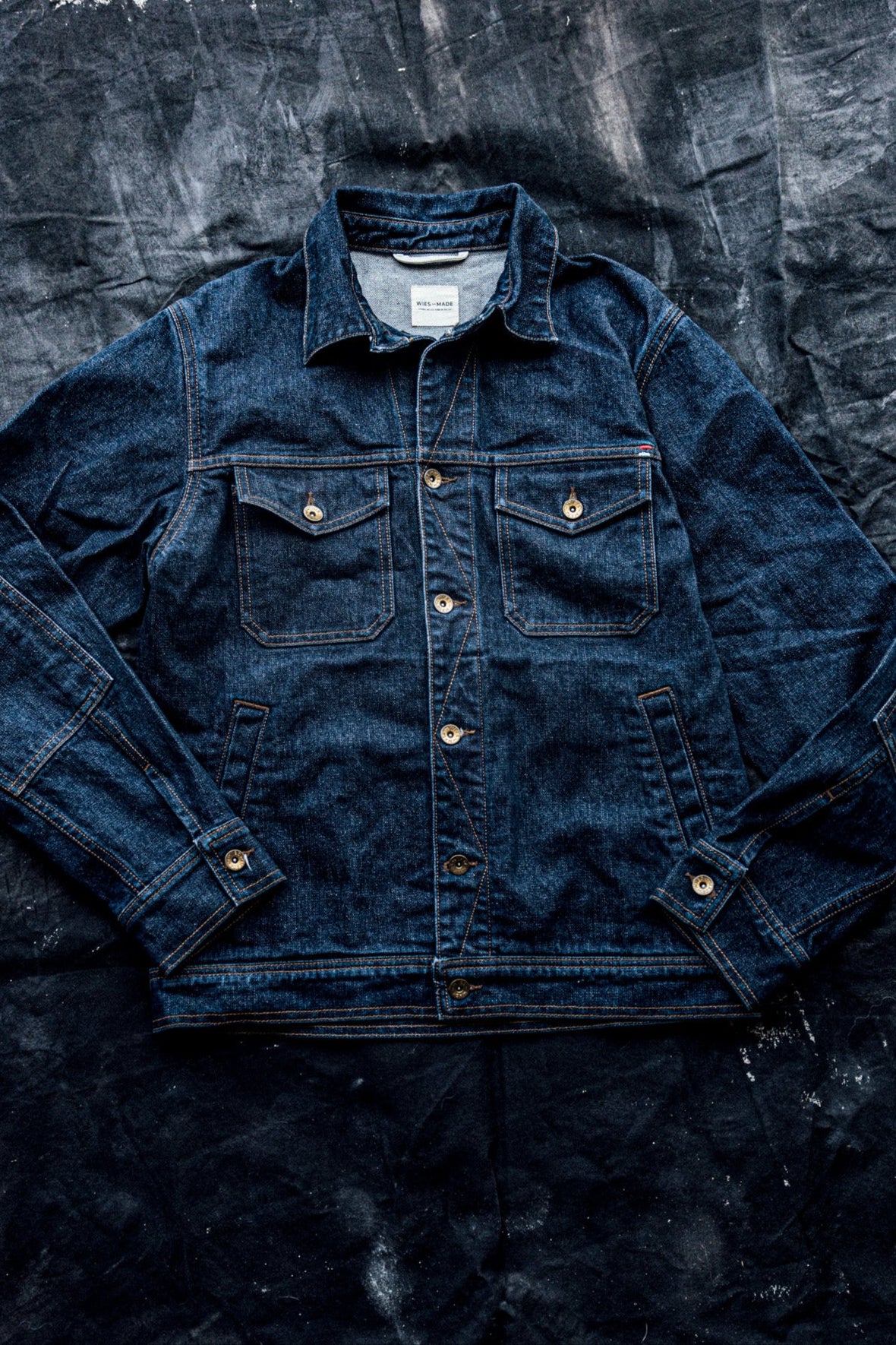 Ocean blue 14oz broken twill denim jacket laid flat, showing chest flap pockets, brass buttons, and contrast stitching.