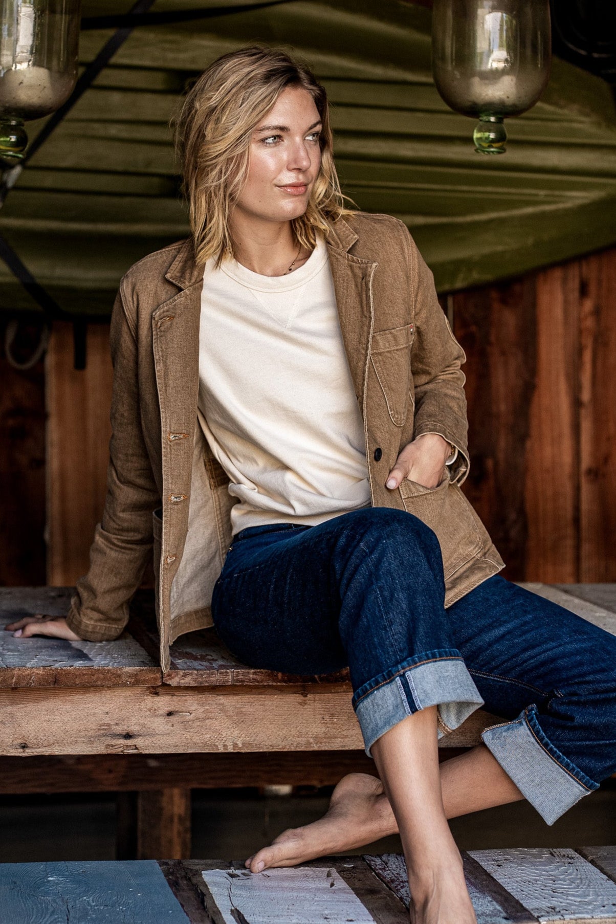 Person wearing wheat denim Scout chore blazer over cream tee, seated on rustic wood.