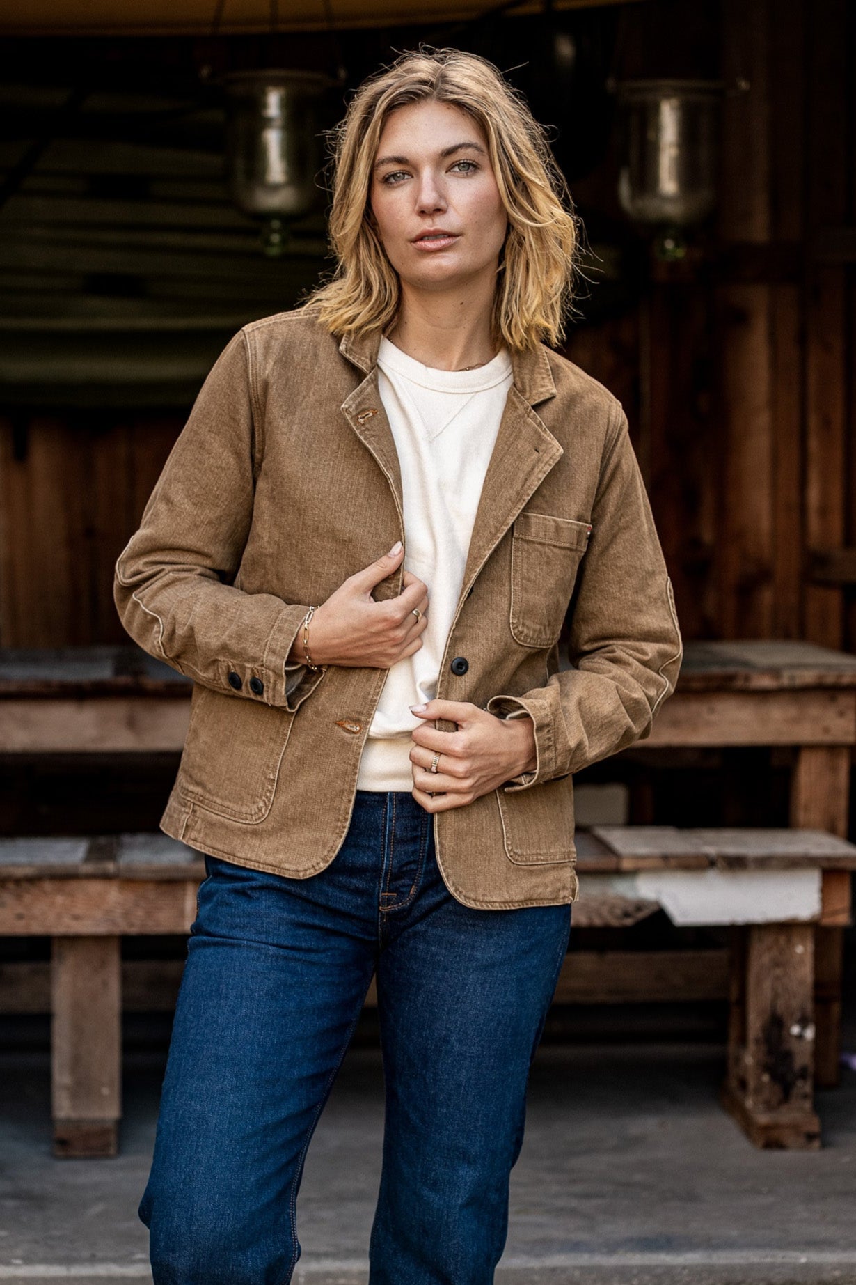 Person wearing wheat denim Scout Blazer over cream tee with blue jeans outdoors.
