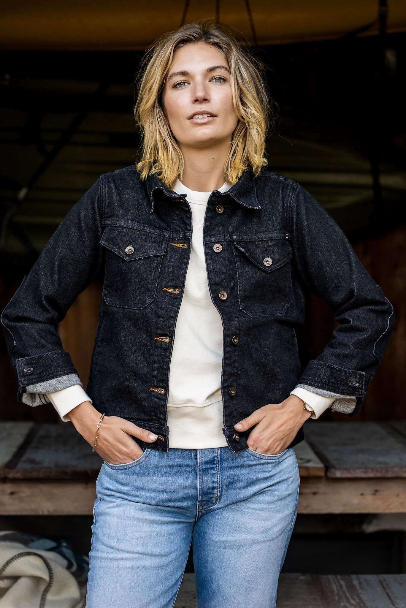 Woman wearing the black broken twill denim Artcher Jacket over a cream tee with light-wash jeans.