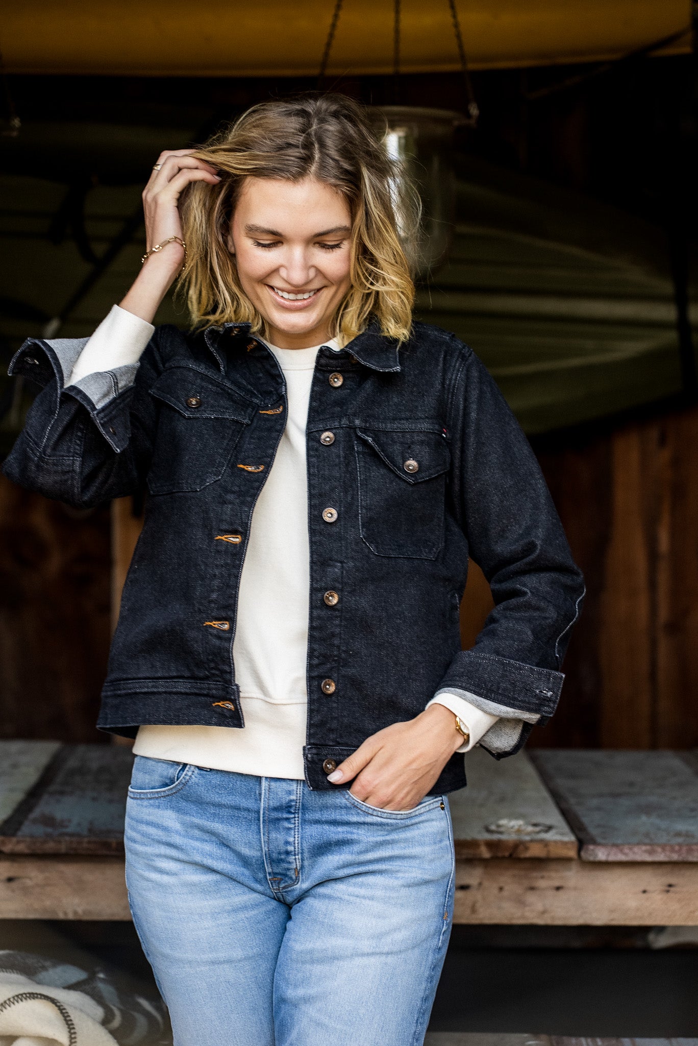 Woman wearing the black broken twill denim Artcher Jacket over a cream sweatshirt and light blue jeans.