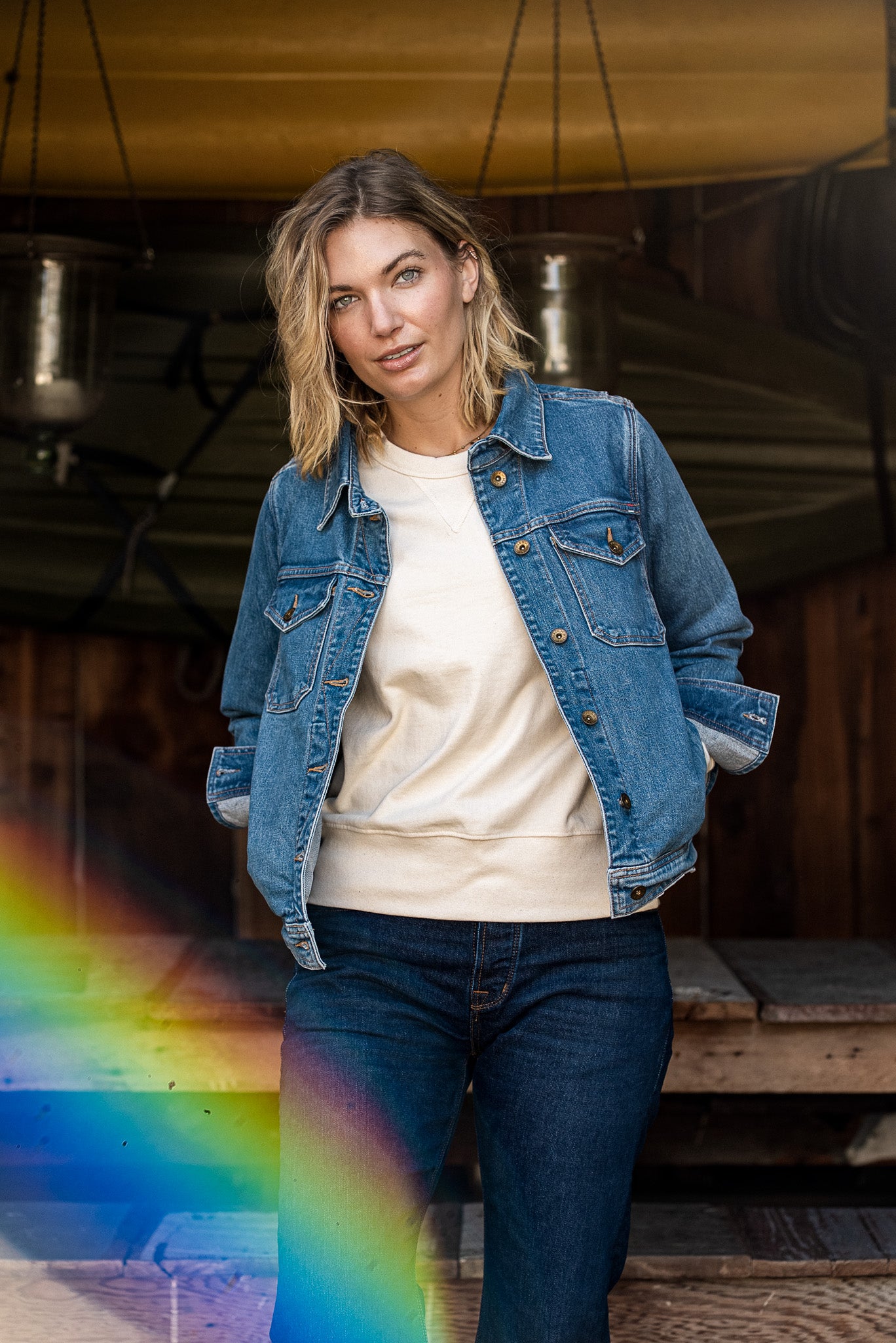 Woman wearing the salt-wash broken twill denim jacket open over a cream sweatshirt and dark jeans.