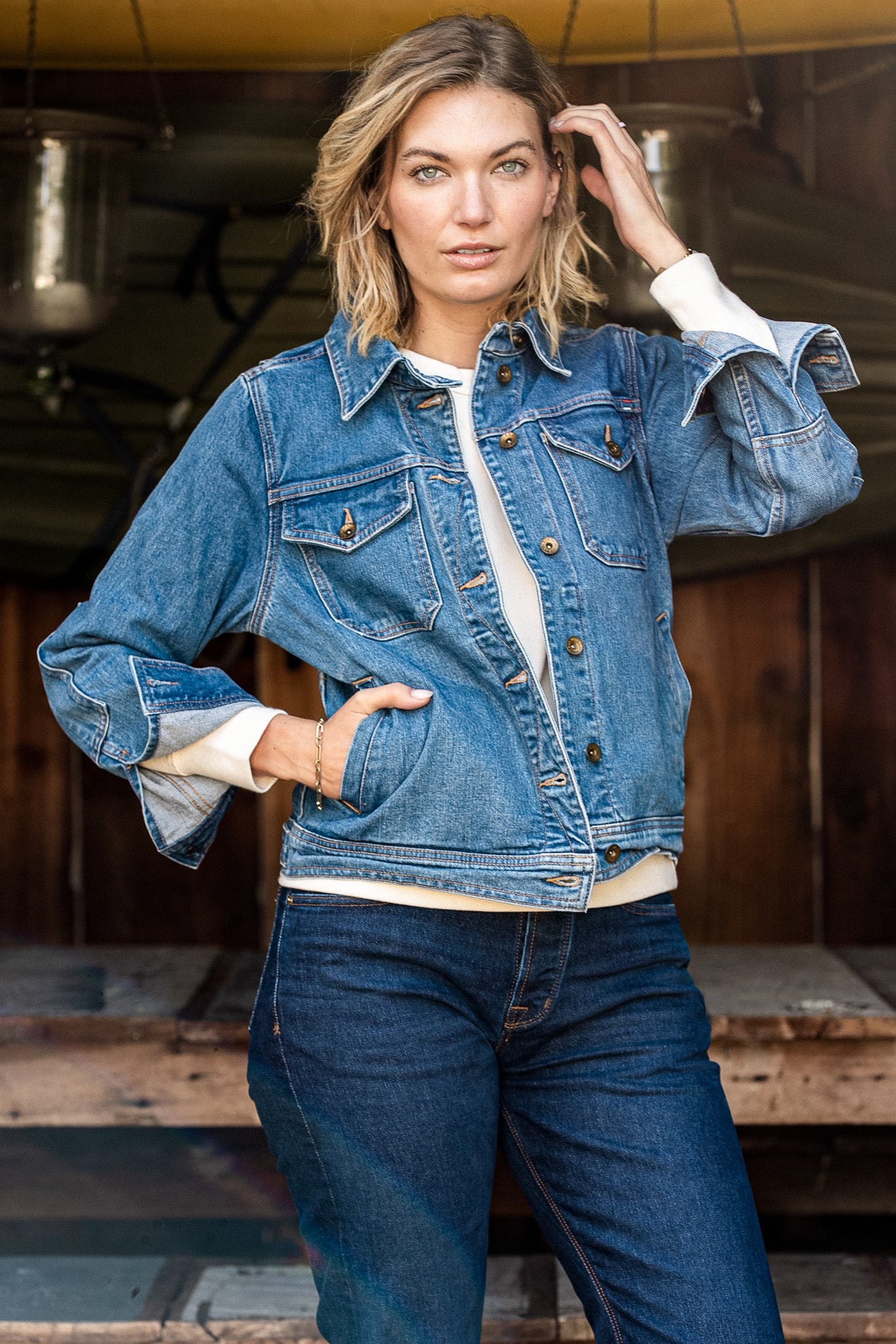 Woman wearing the Artcher broken twill denim jacket in salt wash over a cream sweater with dark jeans.