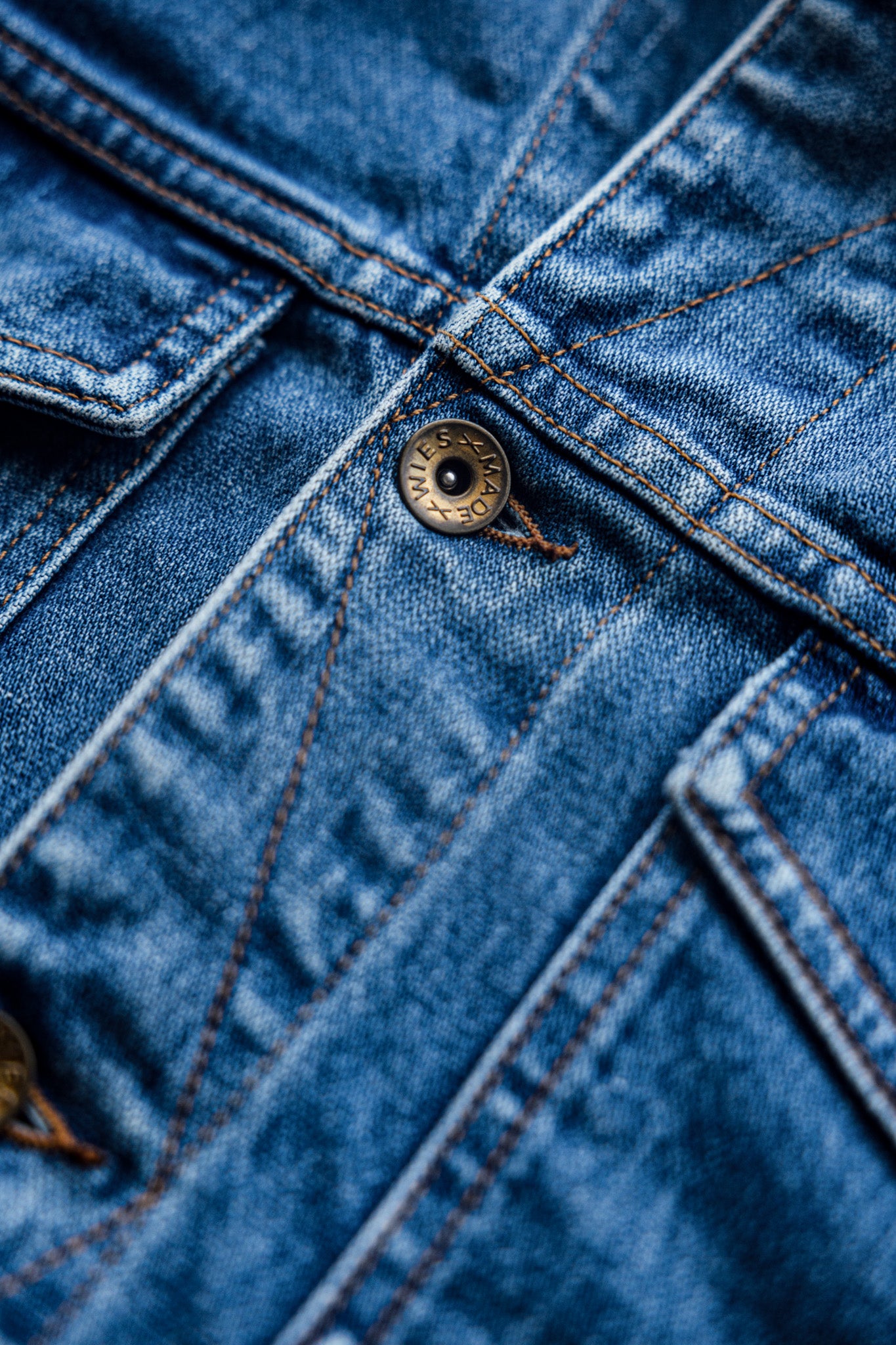 Close-up of the Artcher jacket's broken twill denim with brass WiesMade button and contrast stitching.