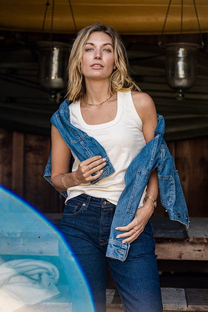 Woman wearing the natural cotton Reyes tank with a denim jacket slipped off her shoulders and dark jeans.