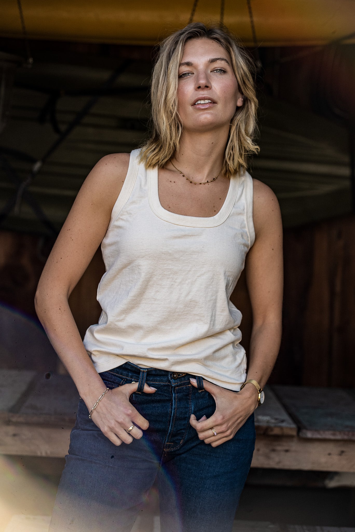 Model wearing a natural cotton Reyes tank tucked into dark denim jeans.