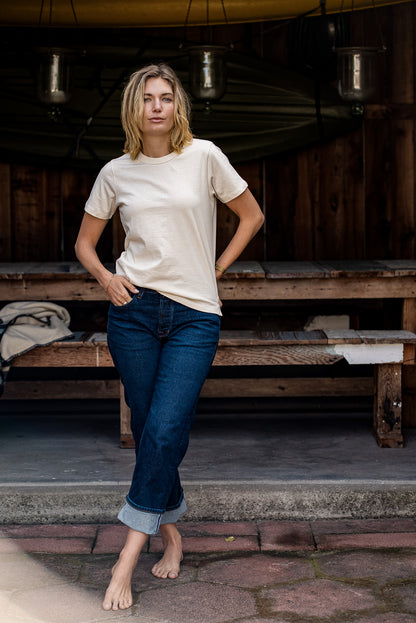 Woman wearing the natural Reyes boxy tee with cuffed dark denim jeans on a covered porch.