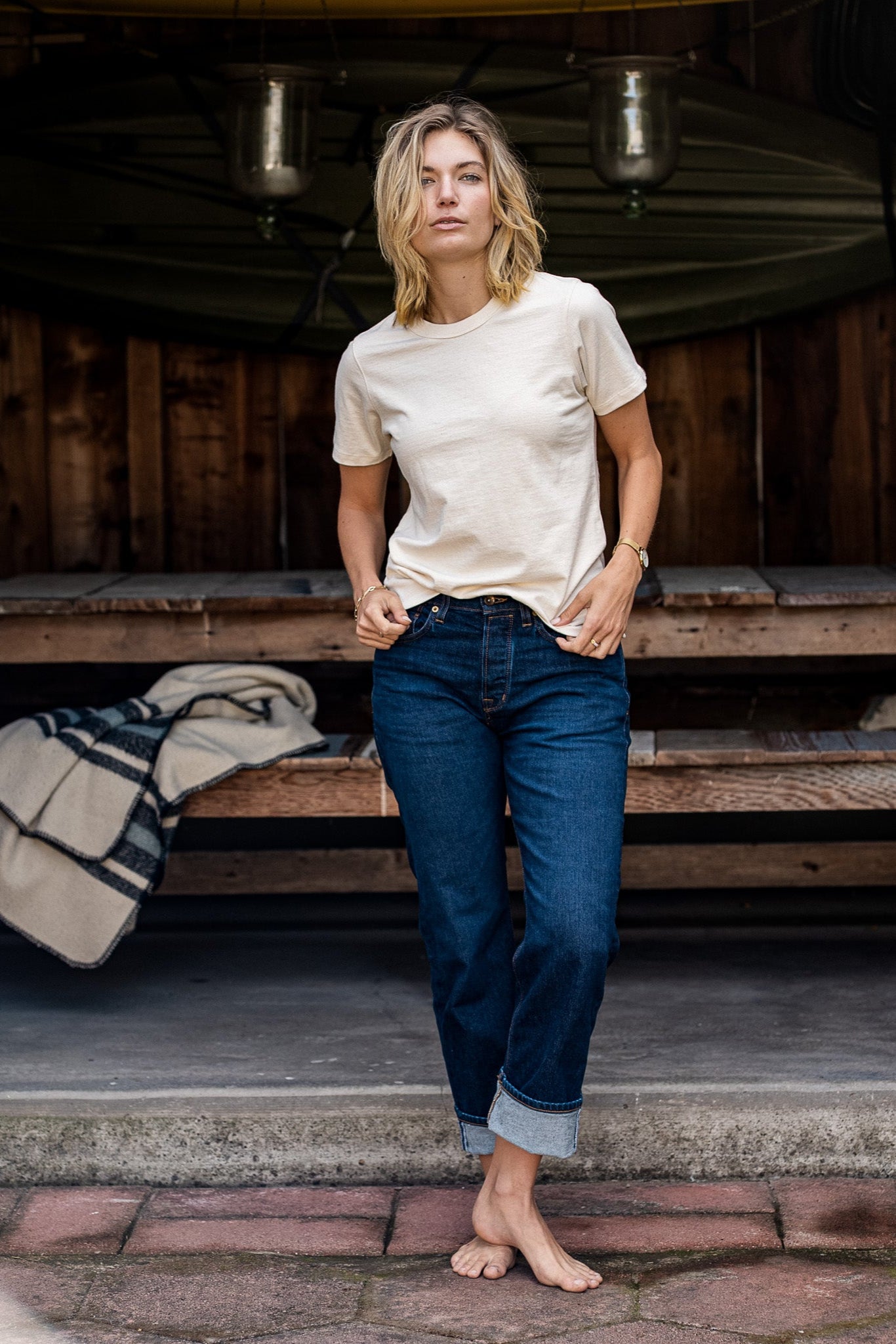 Model wearing the natural Reyes boxy tee with cuffed dark denim jeans on a wooden porch.