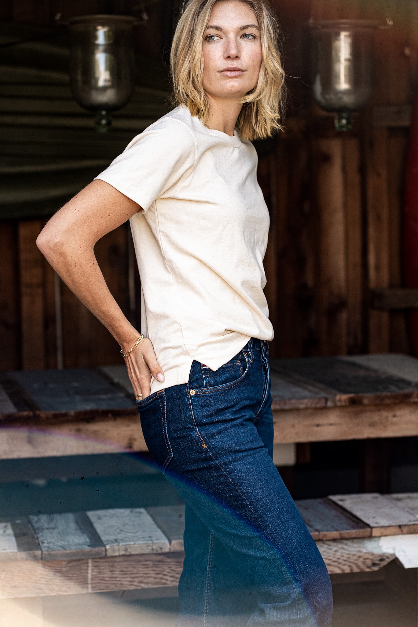 Model in a natural cotton Reyes boxy tee styled with dark wash denim jeans in a rustic workshop.