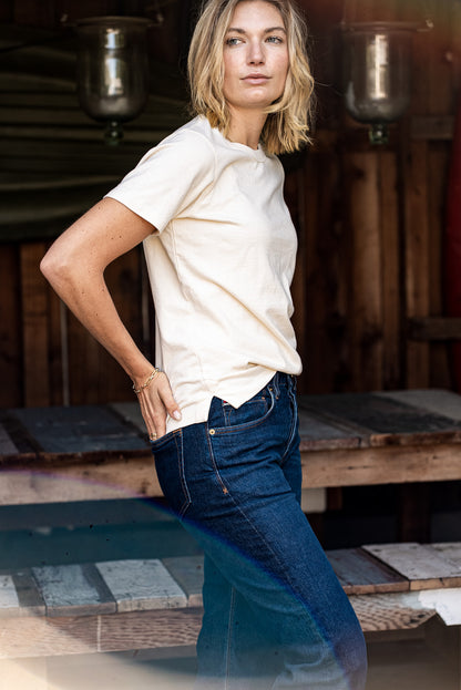 Model in a natural cotton Reyes boxy tee styled with dark wash denim jeans in a rustic workshop.