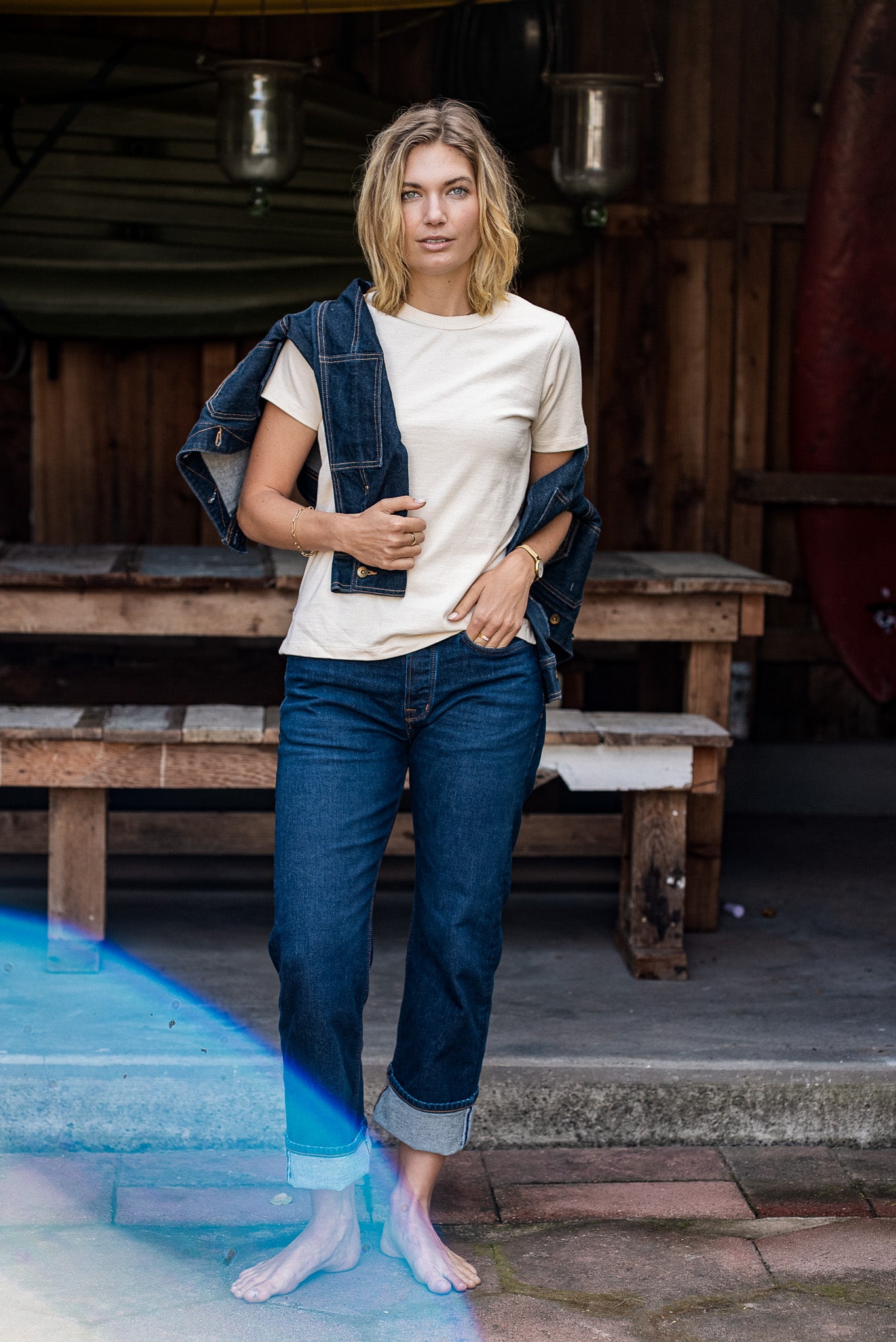 Woman wearing the natural Reyes boxy tee with cuffed selvedge denim jeans and a draped denim jacket outside a wood-paneled.
