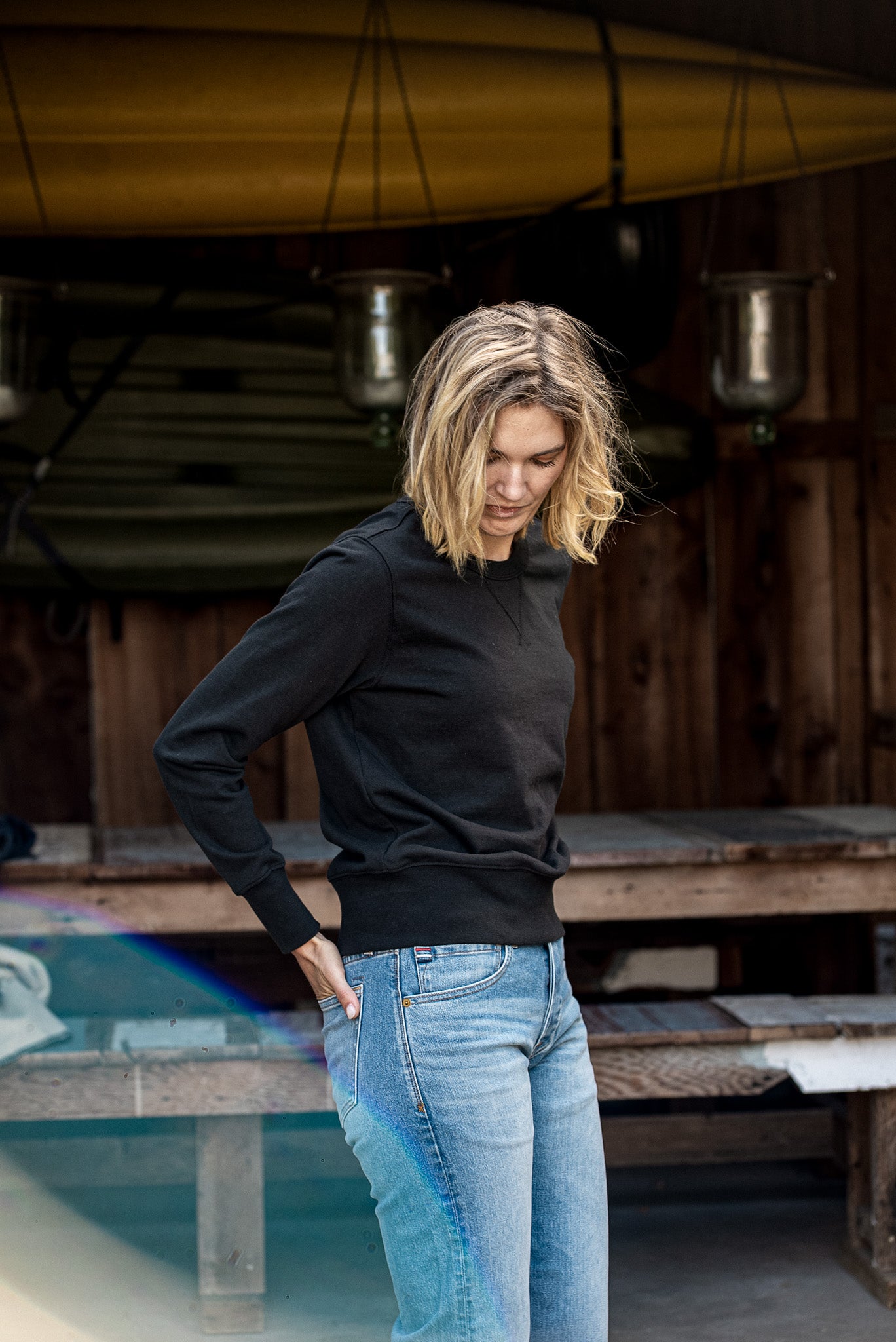 Woman wearing the black Stinson rugby jersey pullover with light-wash jeans in a boathouse.