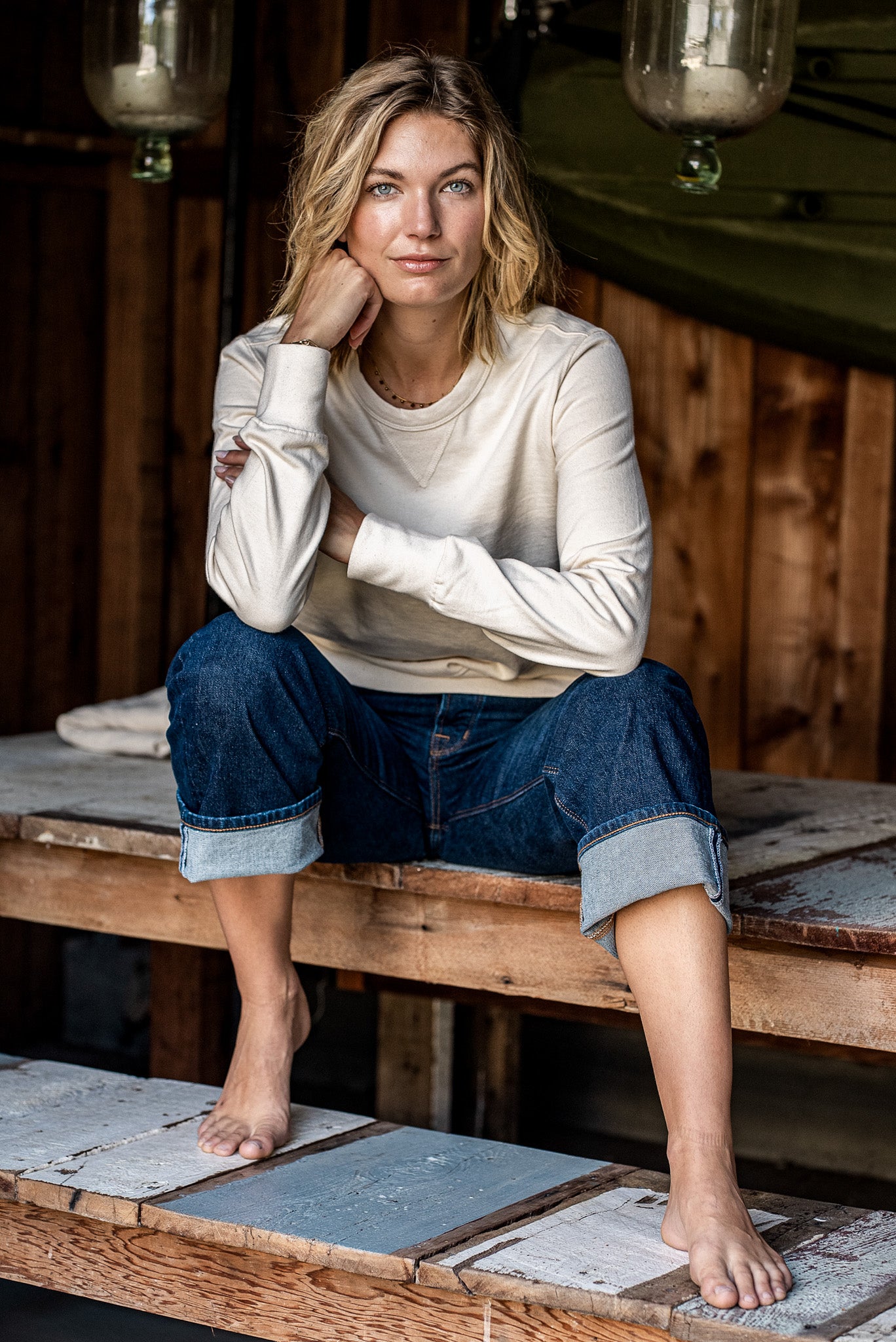 Woman in a natural cream Stinson rugby jersey pullover and cuffed selvedge denim jeans, seated on a wooden porch.