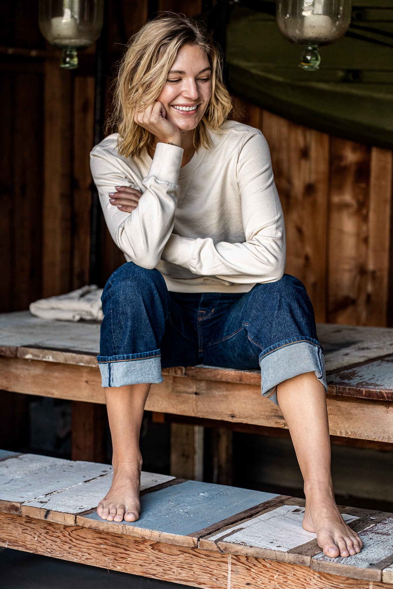 Woman in a natural cream Stinson rugby jersey pullover and cuffed selvedge denim jeans, seated on a wooden porch.