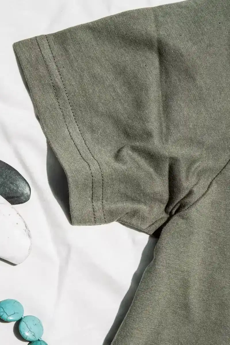 Close-up of olive heavyweight cotton tee sleeve showing double-stitched hem, styled with stones and turquoise beads.