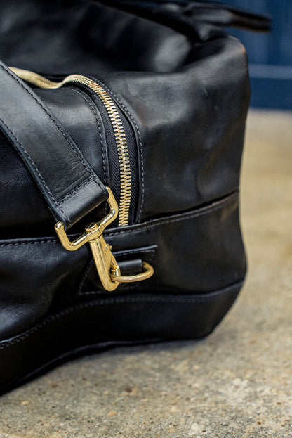 Brass zipper and swivel clasp detail on a black Horween leather weekender bag.