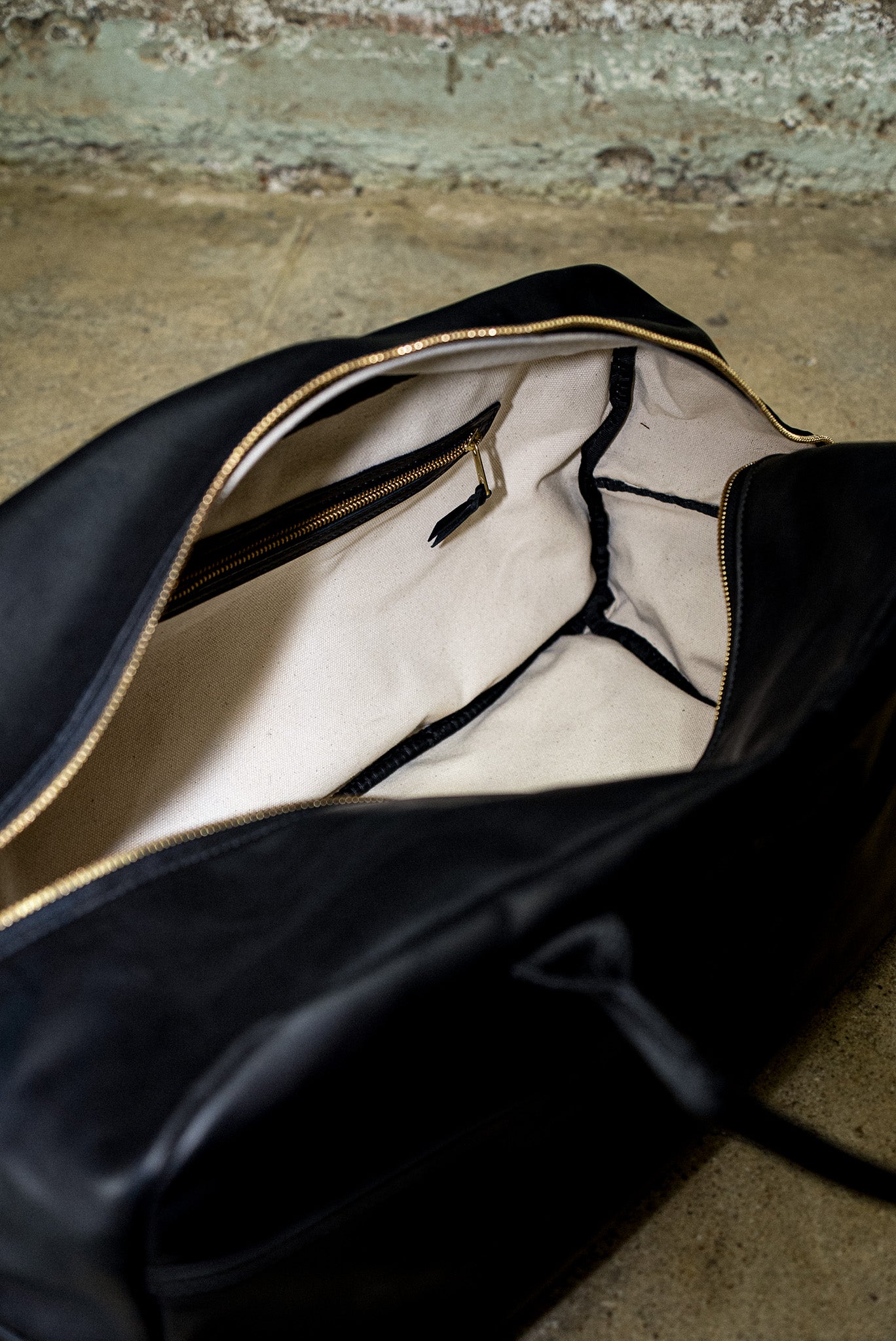 Interior of black leather weekender bag showing natural cotton canvas lining and brass zip pocket.