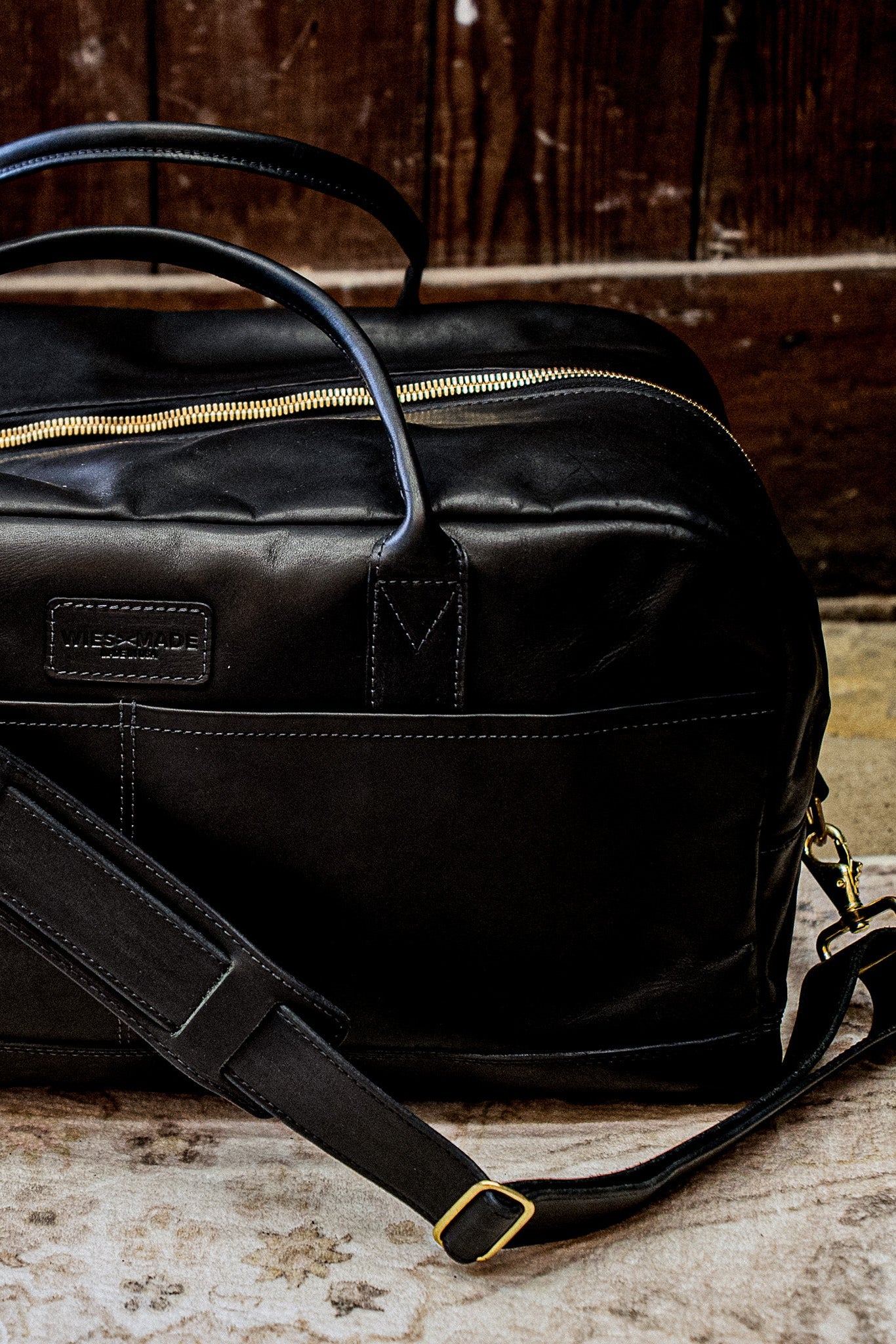 Black Horween leather weekender bag with brass zipper and adjustable shoulder strap.