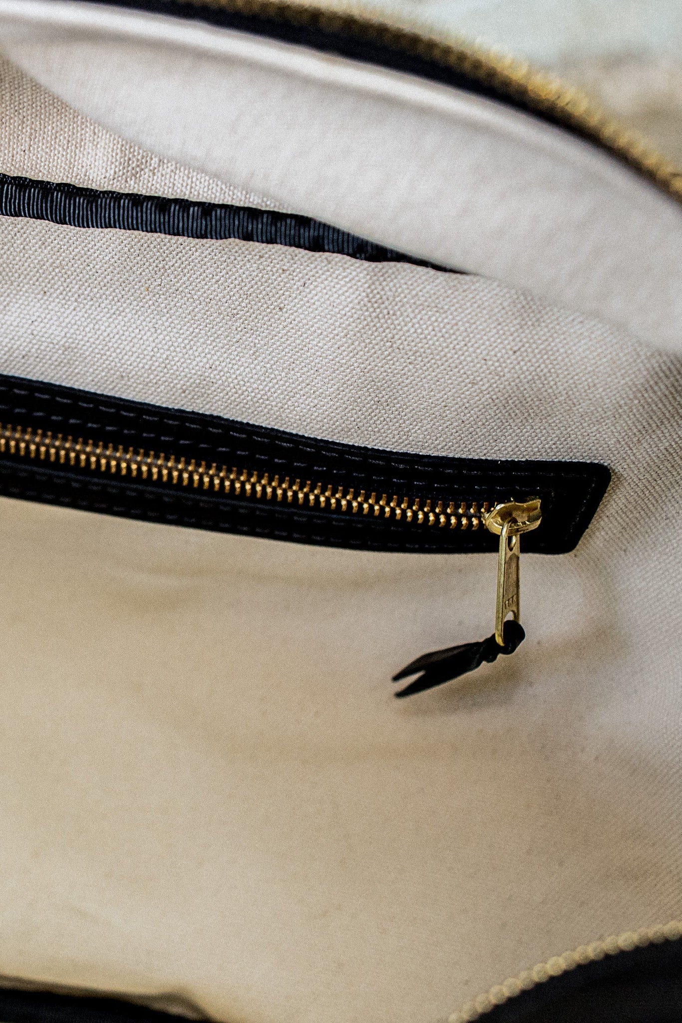 Brass zipper with leather pull on the natural cotton canvas interior of a leather weekender bag.