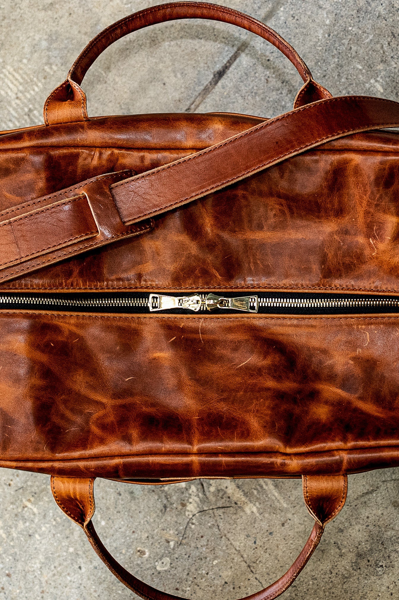 Tan Horween leather weekender bag with brass double-zipper and shoulder strap, top view.