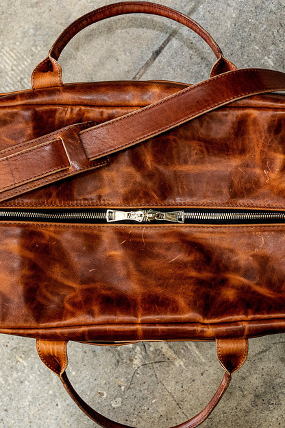Tan Horween leather weekender bag with brass double-zipper and shoulder strap, top view.